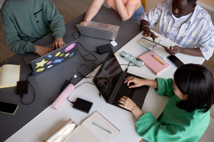 imagem com vários estudantes sentados à mesa com computadores e outros materiais - para ilustrar artigo sobre bolsas de estudo no ensino superior
