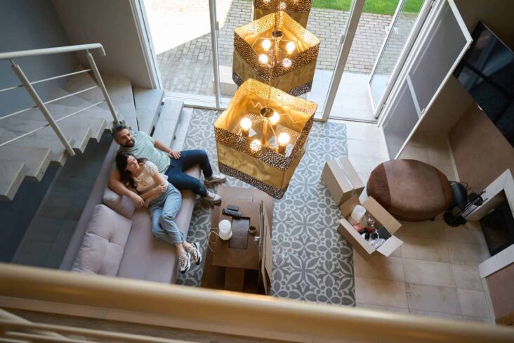 Casal descansa num sofá na sala em casa. Foto tirada de cima, a partir do mezanino a verem-se as escadas.
