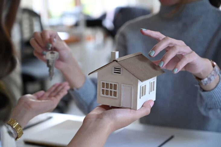 Duas pessoas sentadas numa mesa, uma com uma casa numa mão e outra com uma chave a ilustrar o processo para comprar um imóvel